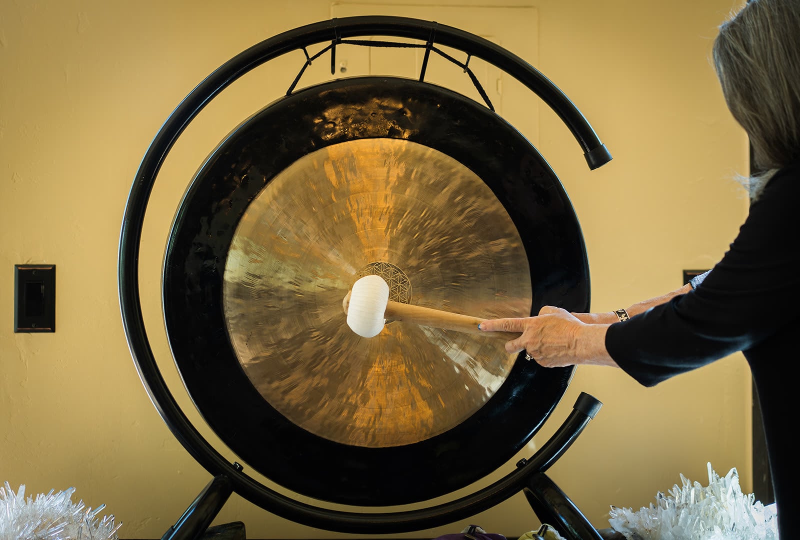 CJ’s hand striking the 36 inch Tibetan gong with a padded mallet, the flower of life engraved at its centre