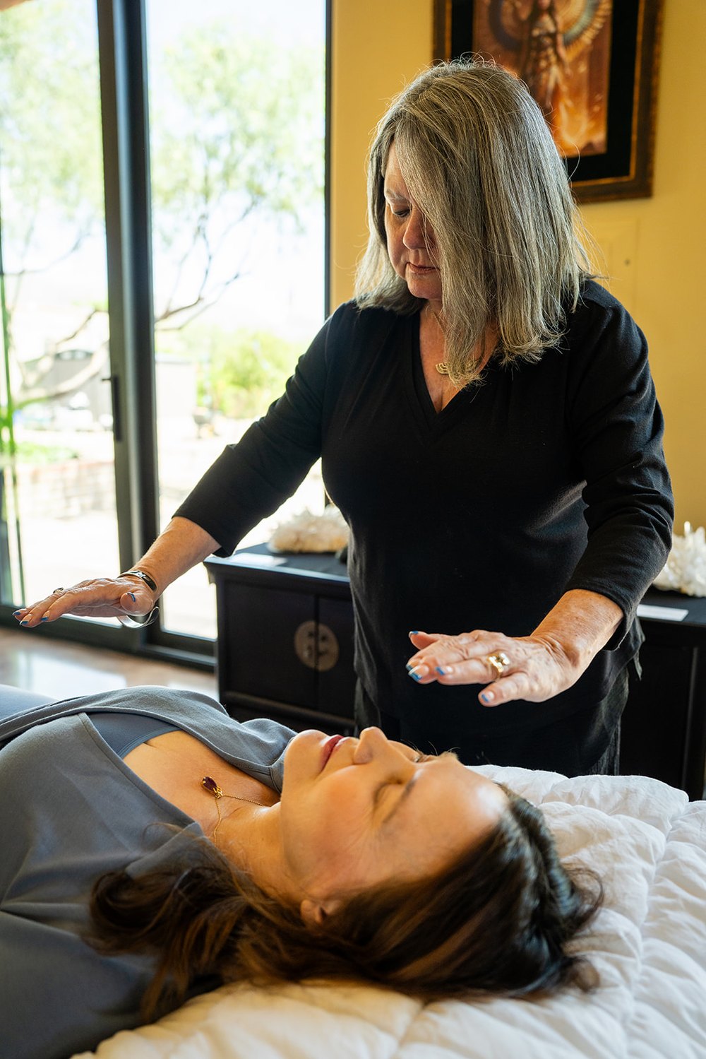 CJ standing at the head of the table with both hands held open above a client resting with her eyes closed