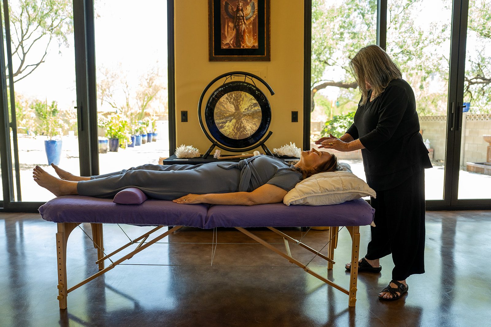 CJ working above a client resting on the table, the gong and glass doors behind them